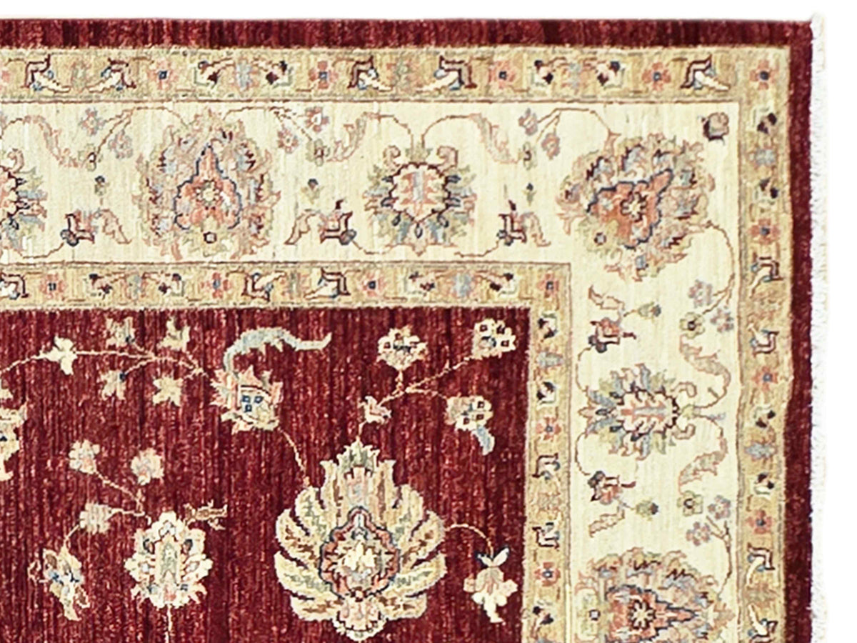 Close-up of red rug field with cream floral motifs and patterned edging