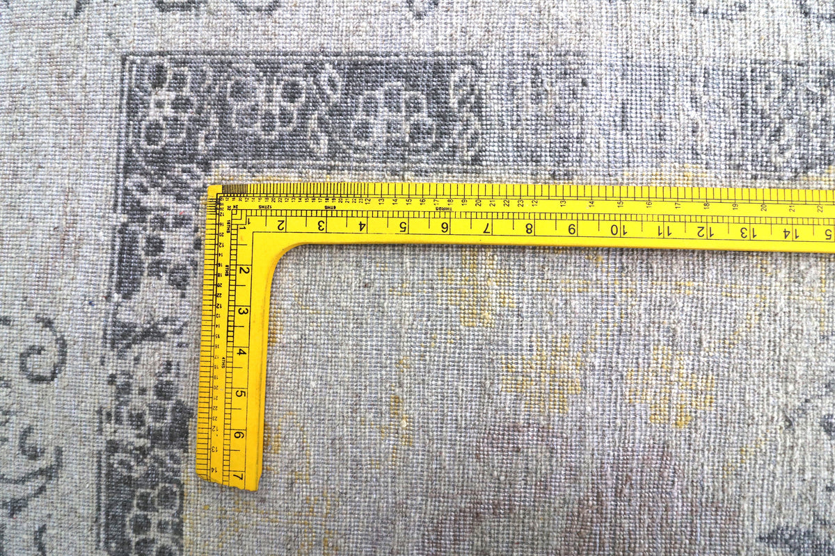 Rug edge detail with measuring tape showing size and stitched border.