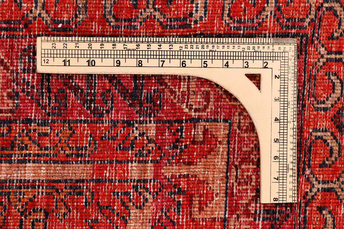 Red patterned rug with measuring tape along edge, detailed weave close-up