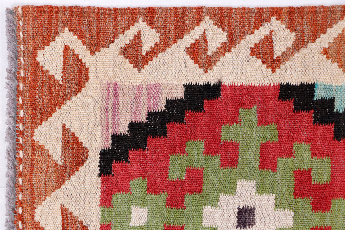 Kilim rug close-up with orange and cream zigzag border and red, green, blue motifs
