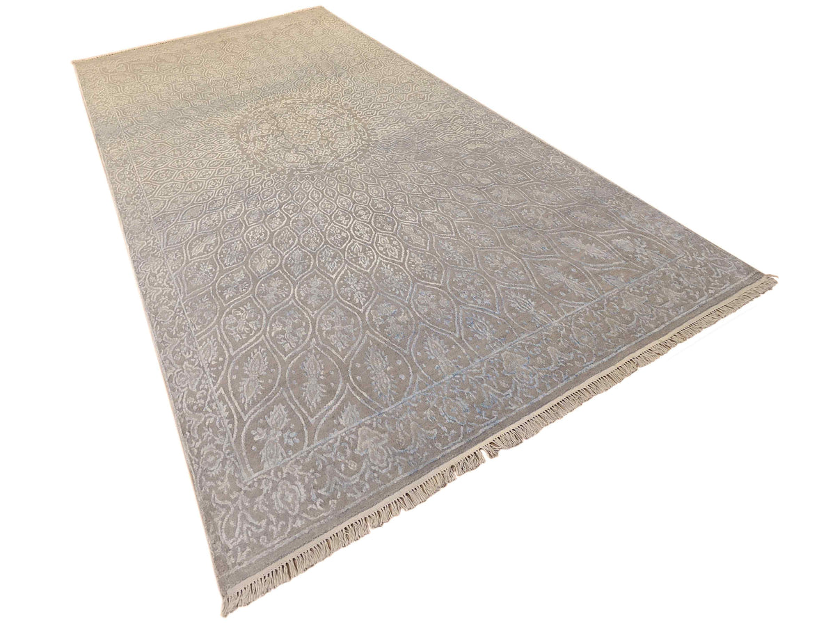Light blue-gray rectangular rug with repeating ornamental design and fringed border.