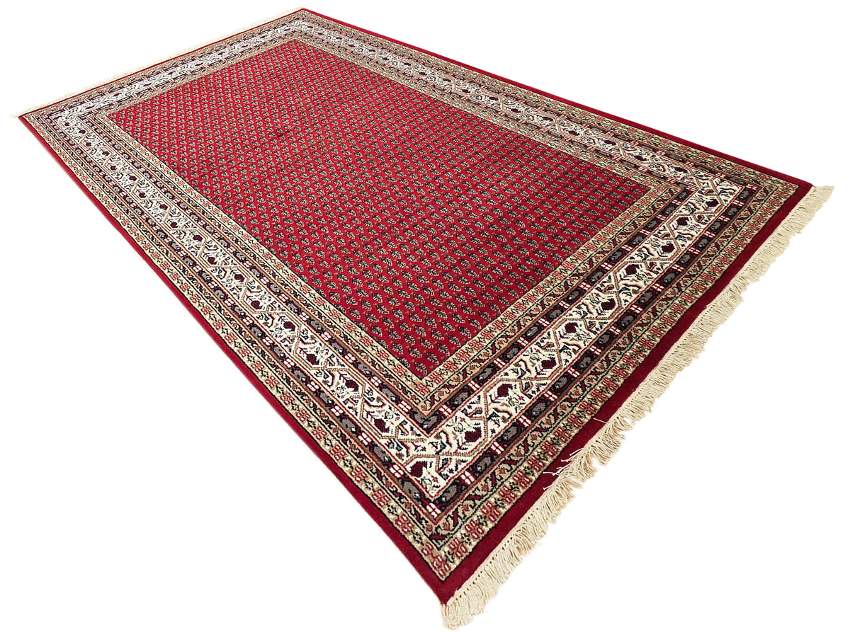 Red geometric rug with decorative frame border, cream accents, and short fringe edges