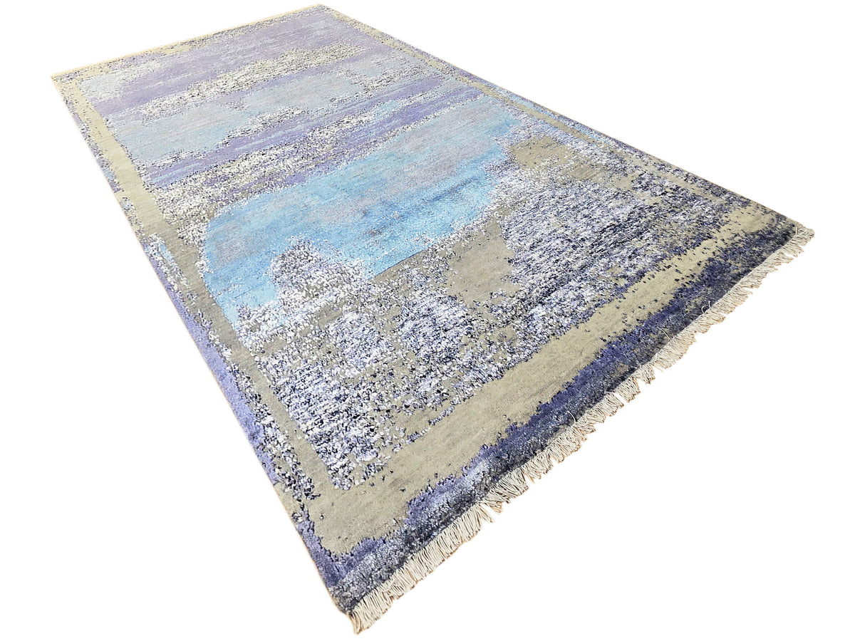 Abstract area rug corner view in blue and beige with violet border; fringed ends