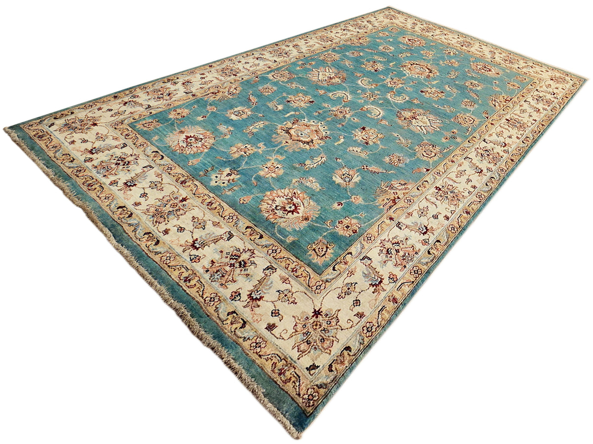 Turquoise area rug with cream corner florals and patterned border, fringed edges