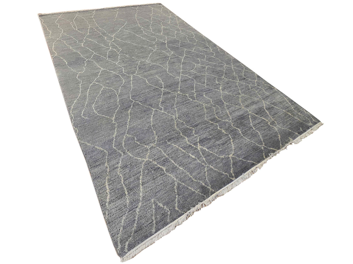 Grey rug shown at an angle with crackled trellis pattern and fringed edges.