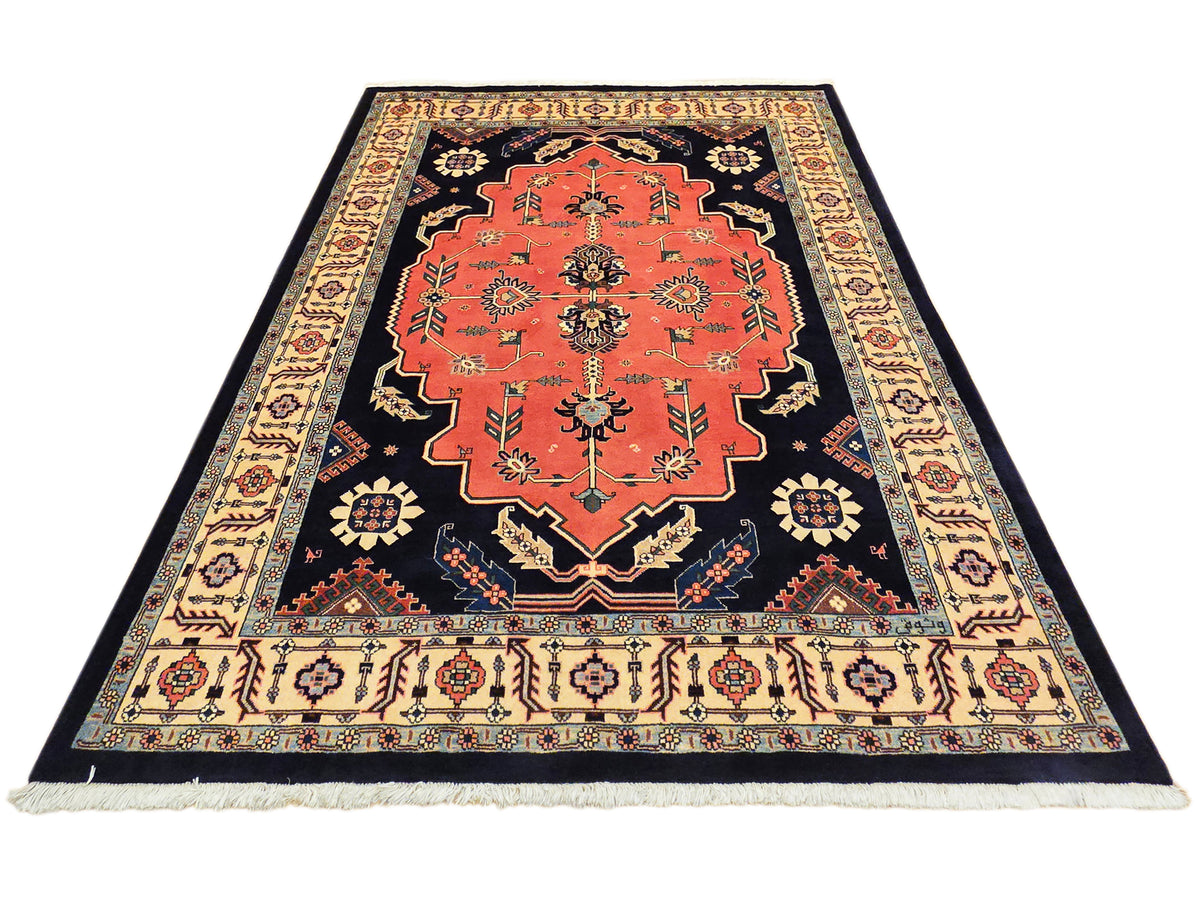 Wide rectangular rug with red medallion on navy field, cream border, and fringe edges