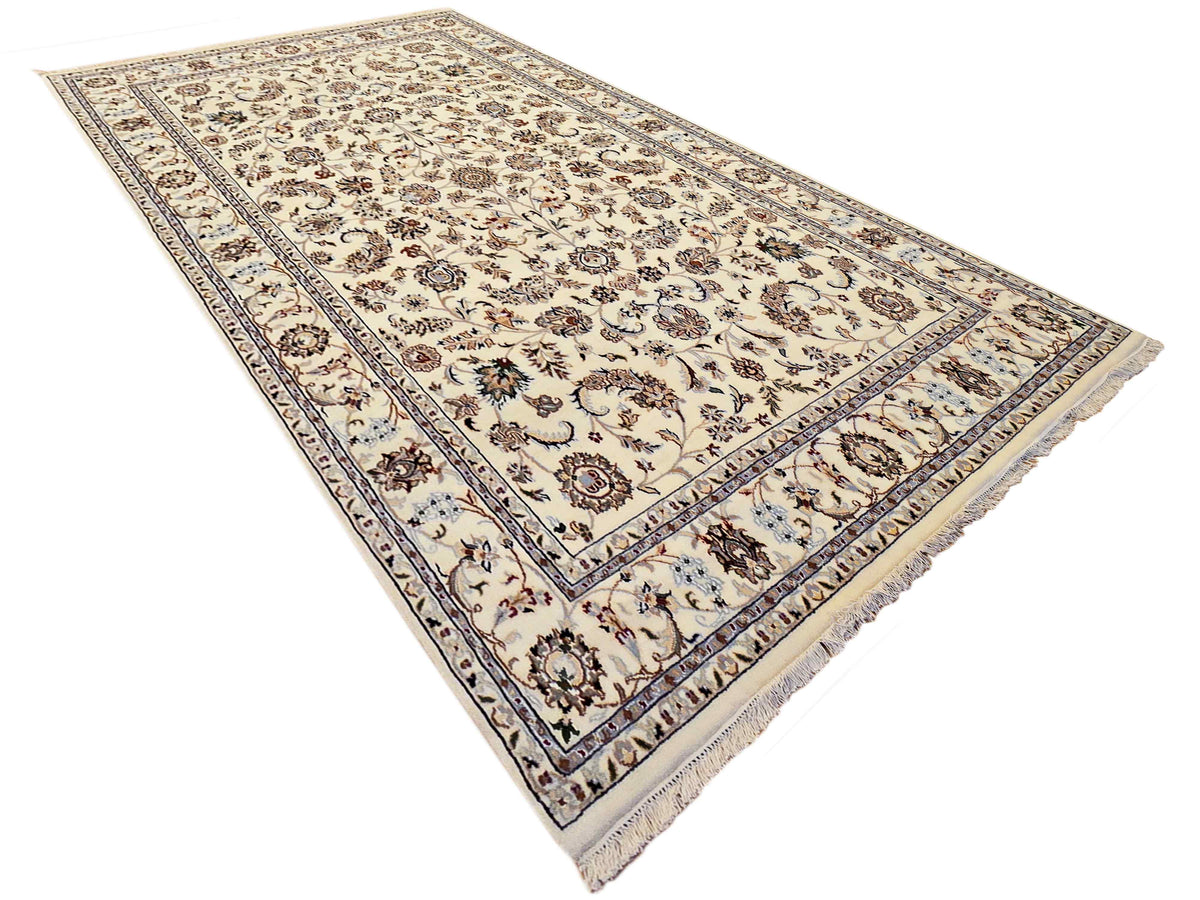 Corner view of cream rug with ornate floral field and blue geometric frame, fringed ends