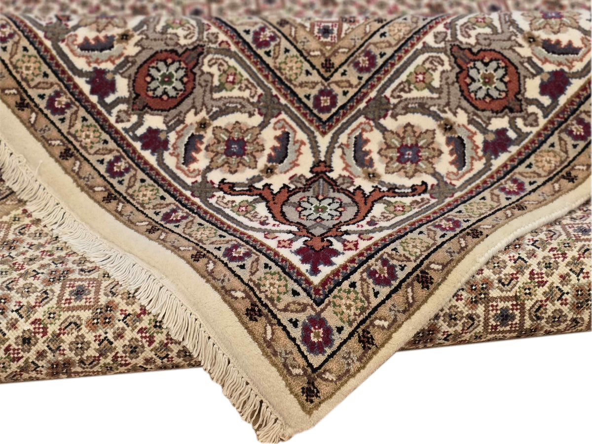 Corner of beige rug with floral diamond pattern and cream fringe