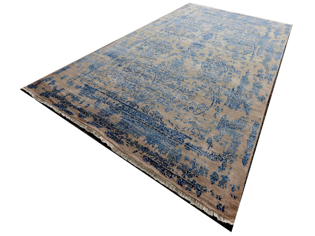 Rectangular rug corner view, light beige base with blue scrolling motifs and fringe edges.