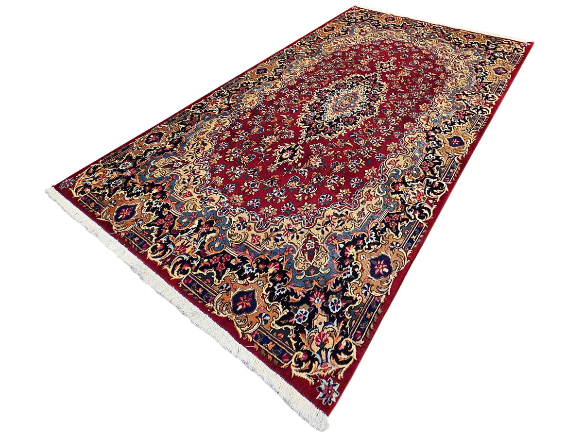 Red patterned rug with detailed border and floral medallion, angled view