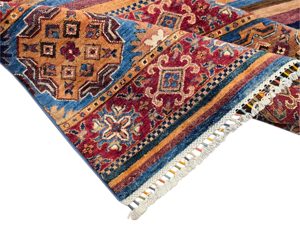 Diagonal view of multicolor rug with central medallion, striped bands, and white fringe