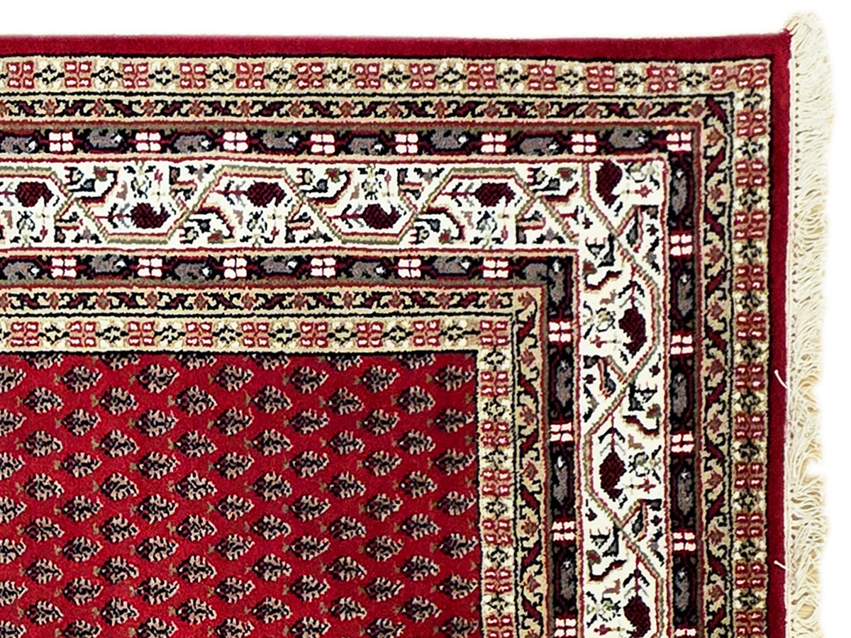 Red rug corner view with cream border details and cream fringe along the edge