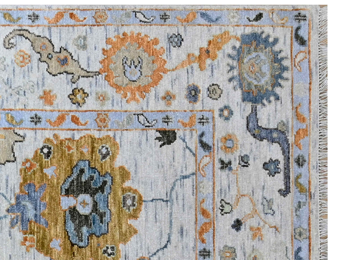 Oushak-style rug close-up with light blue pattern, orange medallion, cream rosette details on border
