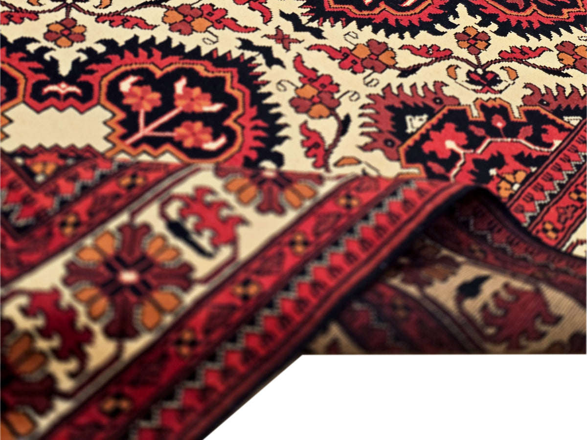 Close-up of Afghan rug pattern: cream ground with red, navy, and orange floral geometric details.