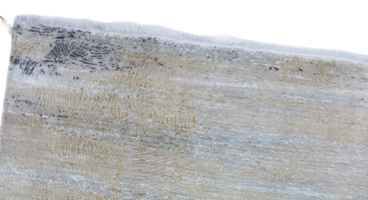 Close-up of rug border showing light blue and cream texture with short fringe.