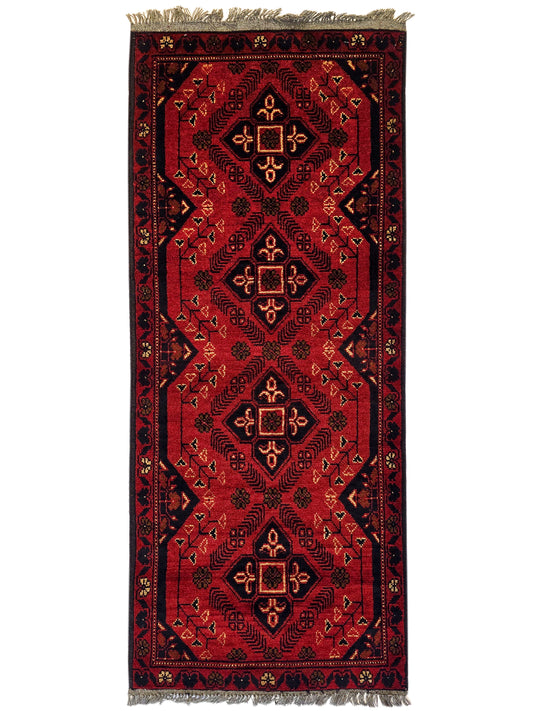 Red vertically oriented geometric rug with central diamond motifs and fringed top