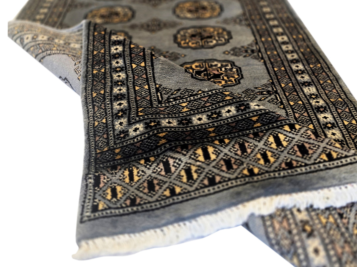 Corner view of patterned rug with dark geometric bands, medallion motifs, and short fringe