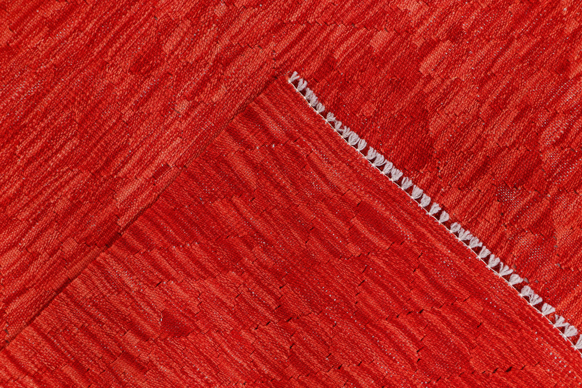 Red kilim rug corner with white-trim fringe and diagonal flat-weave pattern