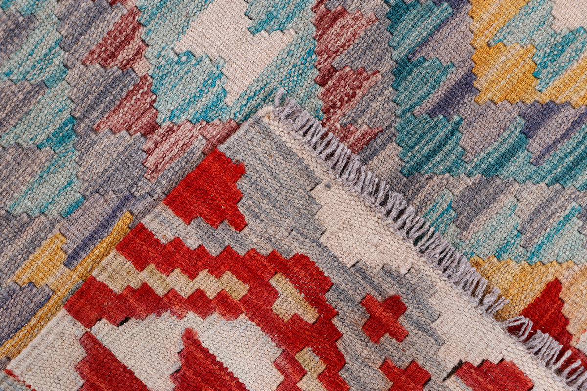 Kilim rug close-up with fringe and geometric pattern in red, teal, blue, and grey