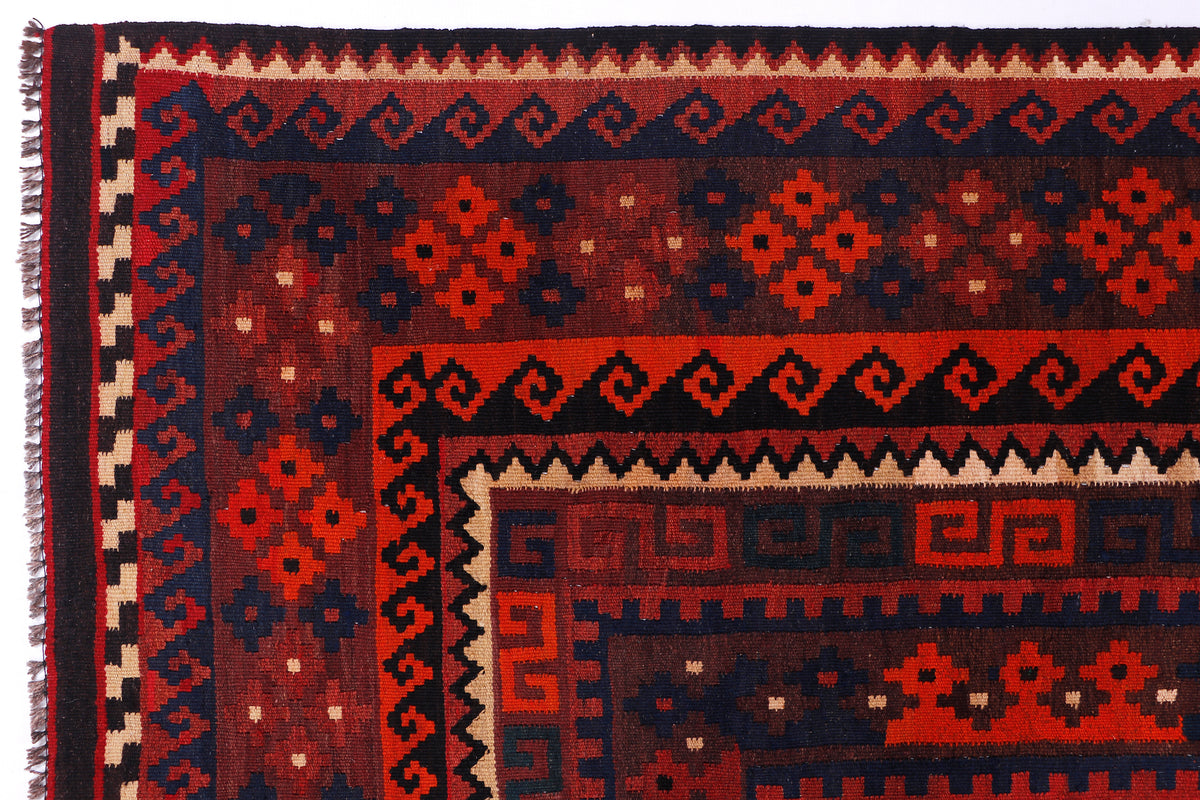 Crimson red kilim rug corner with navy and cream geometric pattern, fringed edge