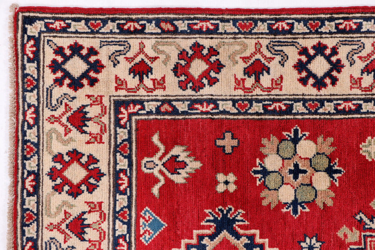 Red rug section with cream and navy border and floral cross motifs, tight crop