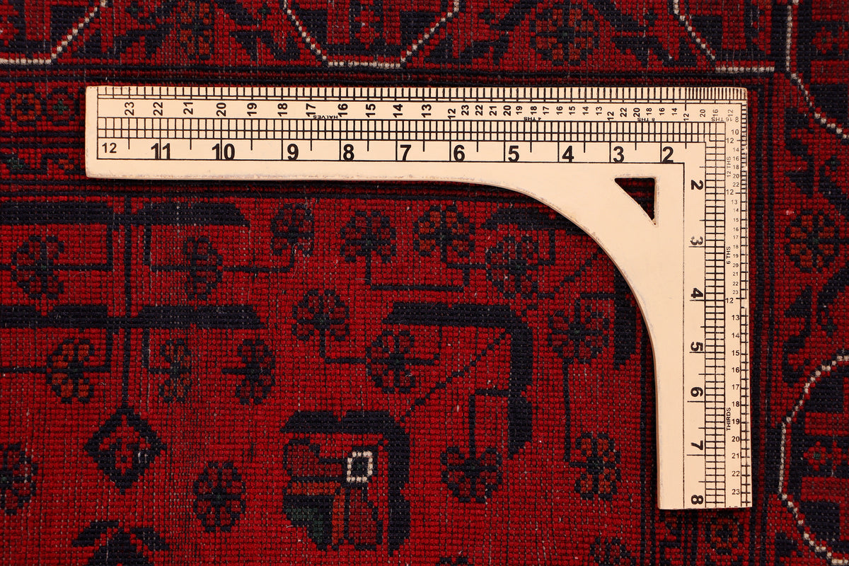 Red rug close-up with geometric motifs; tape measure along the border