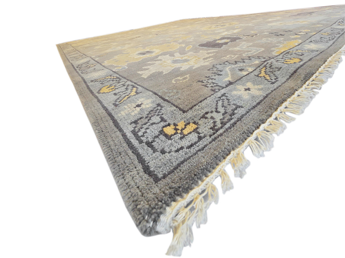 Oushak rug corner with gray and yellow motifs, decorative border and white fringe.