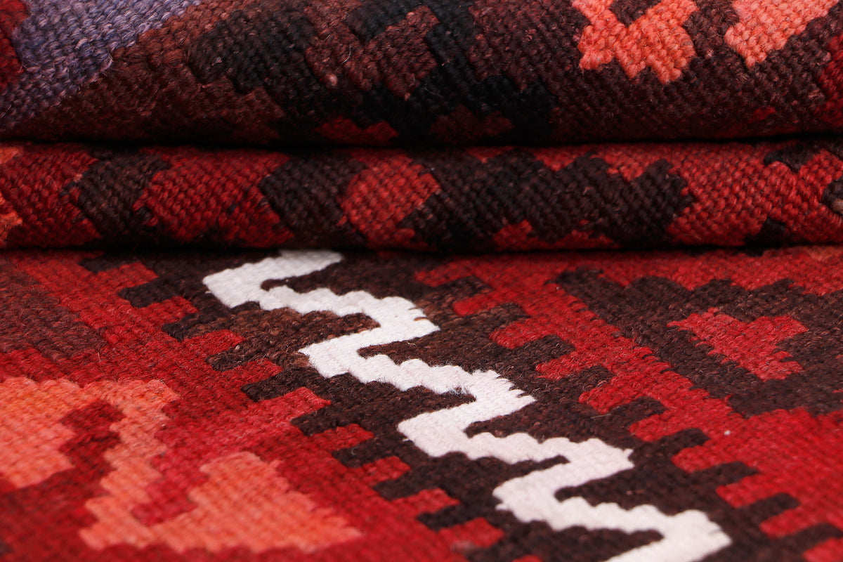 Red kilim rug close-up with geometric white motifs and dark border