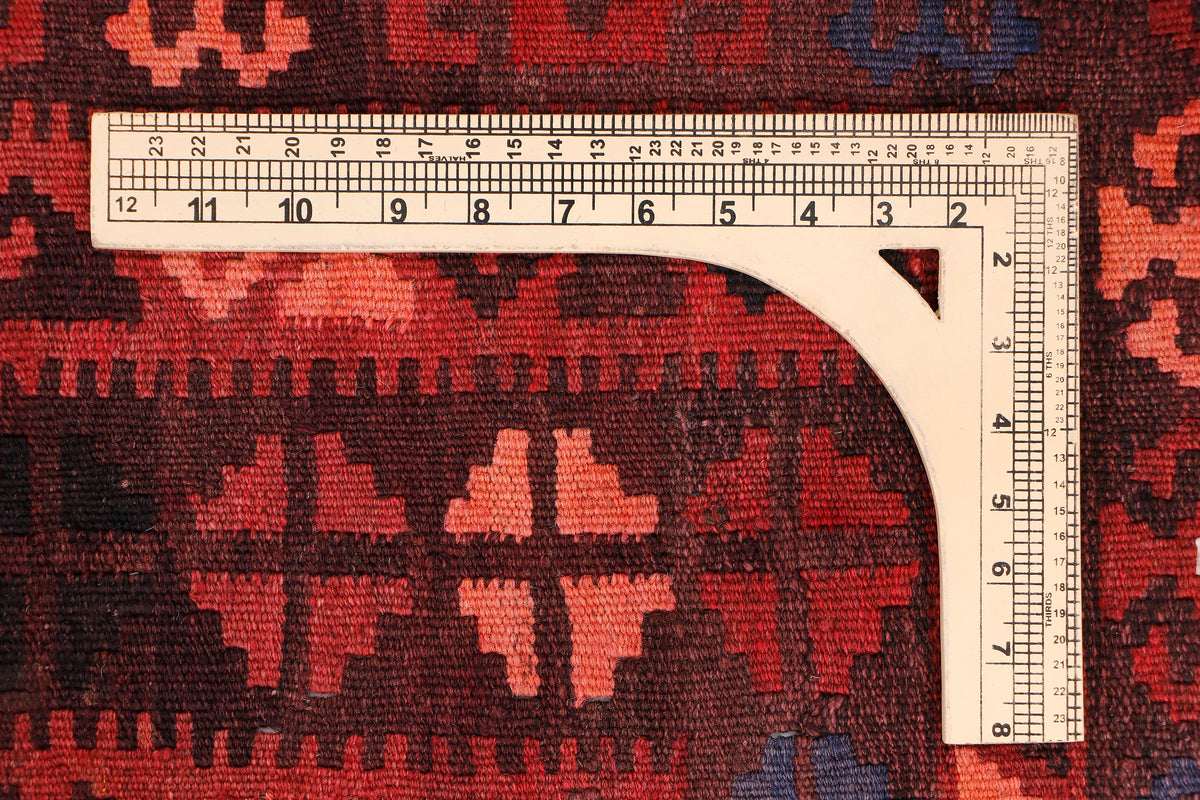 Red kilim rug with measuring tape along an arched edge; geometric pattern