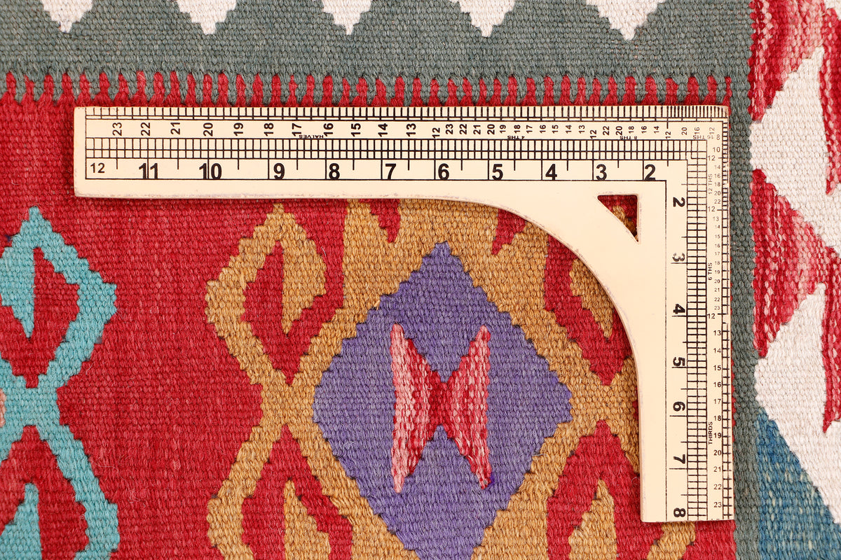 Kilim rug close-up with geometric motifs in red, beige, blue, with measuring tape