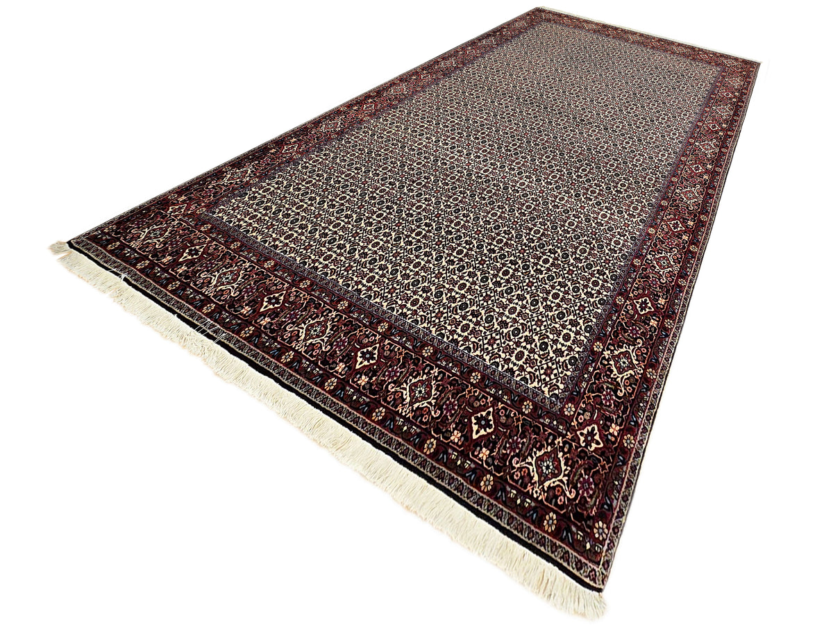 Bidjar rug angled view with beige geometric field, dark red border, and fringe ends