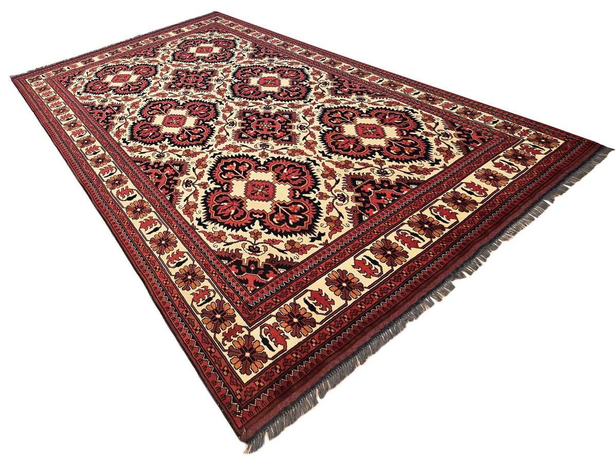 Afghan rug on white background with cream field, red and dark floral medallions; short fringe trim.