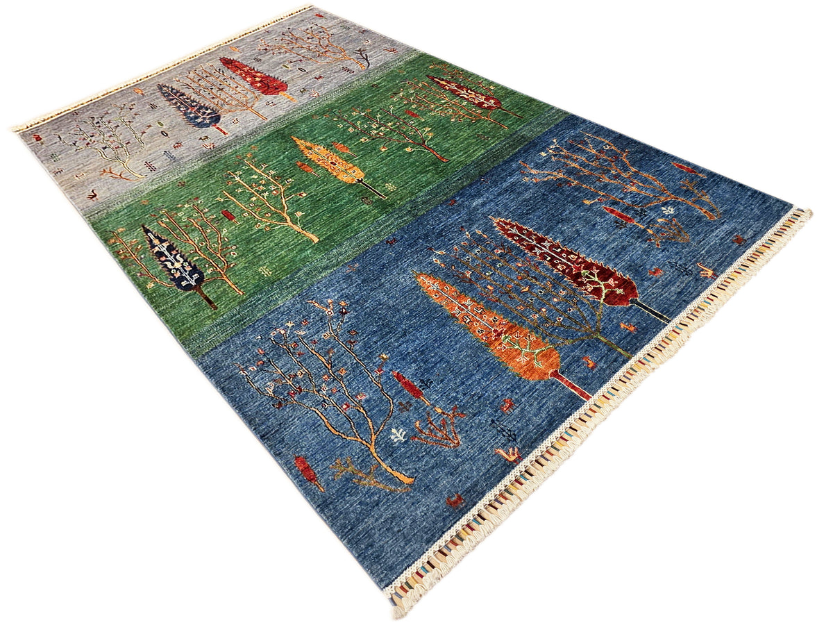 Angled view of blue and green area rug with orange tree motifs and fringed border.