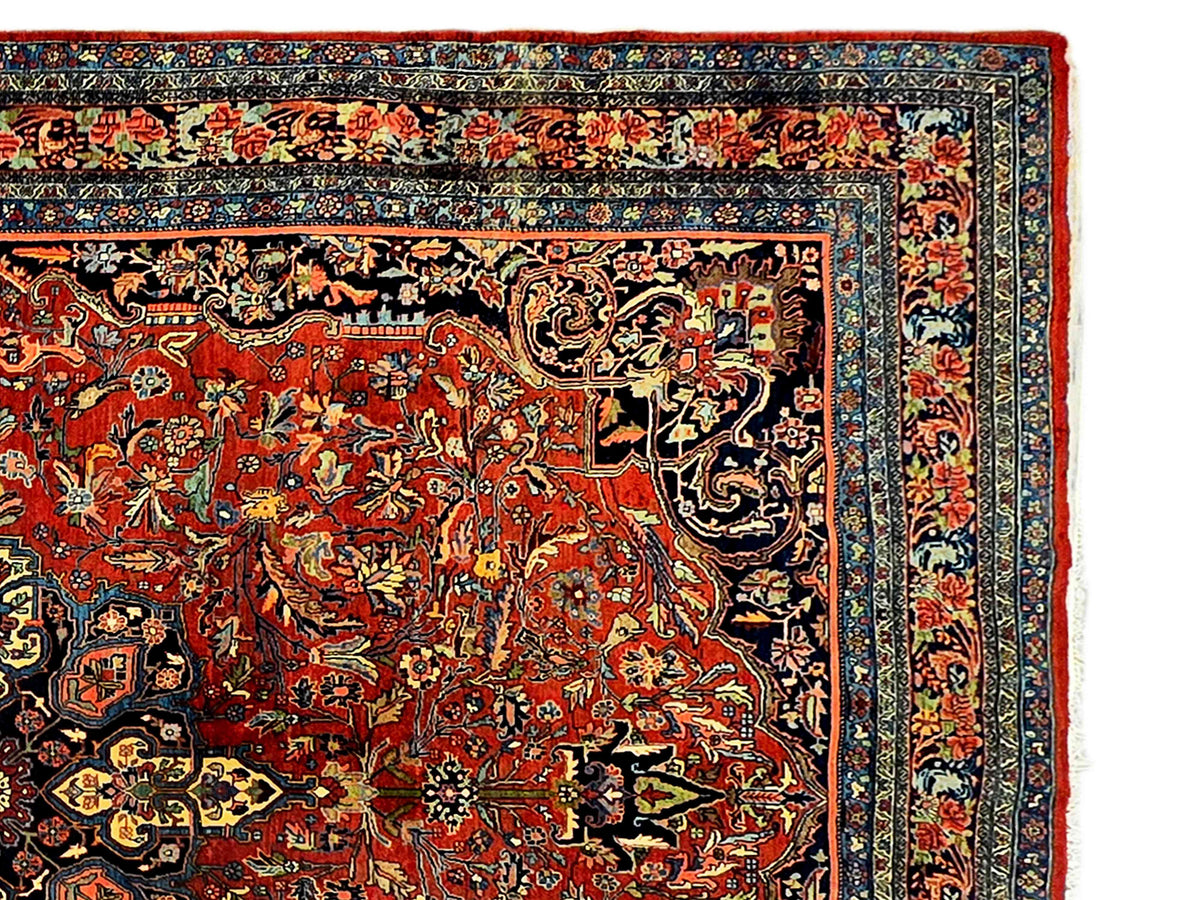 Close-up of red rug with navy border, scrolling floral patterns, and medallion details