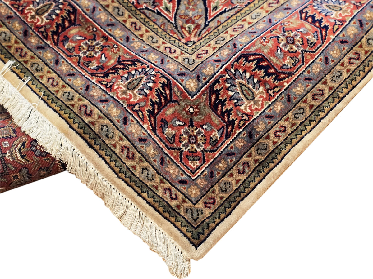 Rug corner close-up with red and blue medallion pattern and cream fringe.