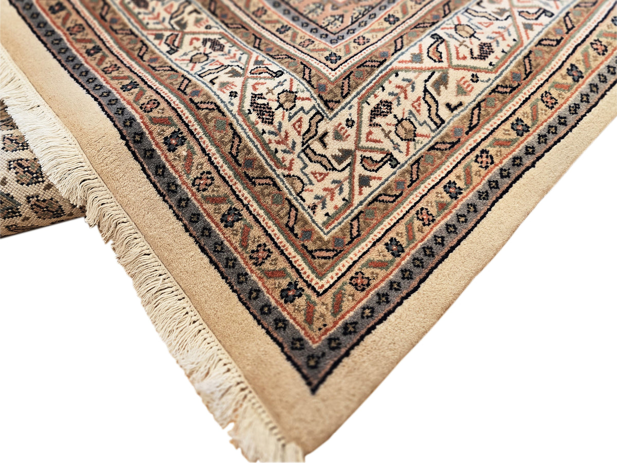 Corner detail of patterned area rug with cream ground, navy stripes, and fringe