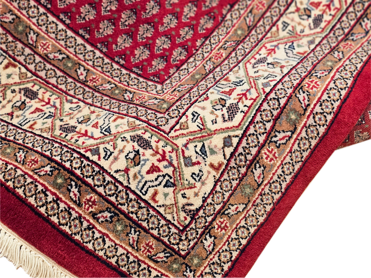Red and cream rug close-up with intricate banded border and woven fringe.