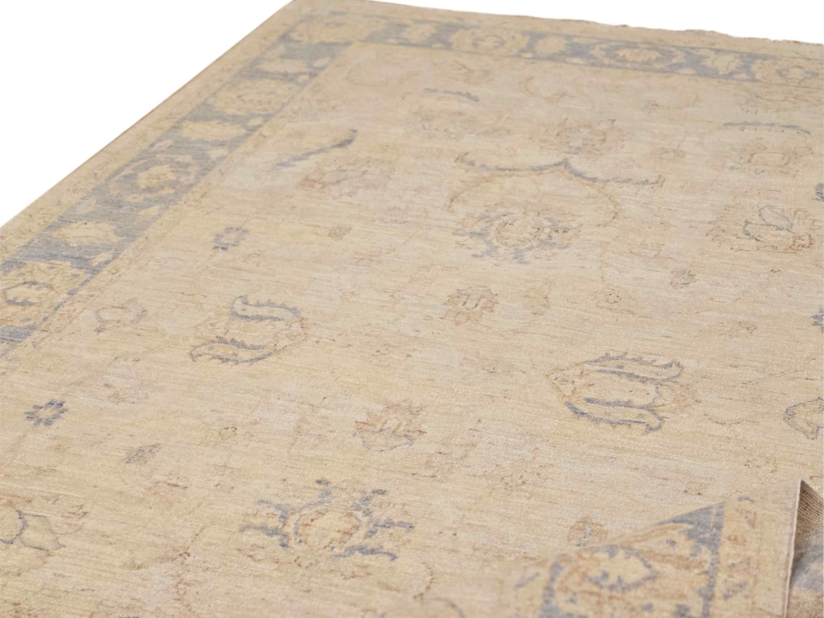 Close-up of beige area rug with light blue vine motifs and distressed texture