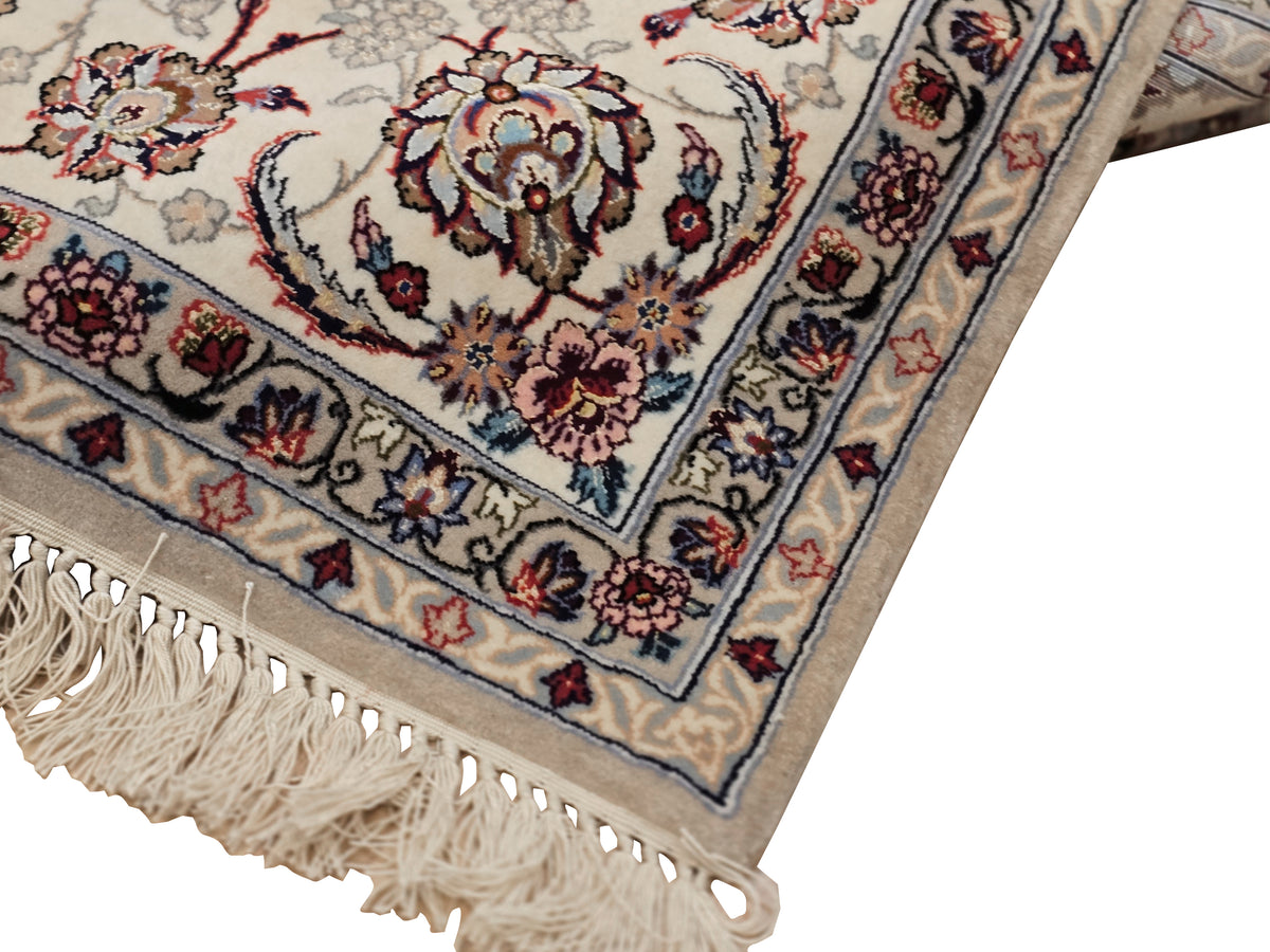 Isfahan rug corner: cream background with blue-red motifs and long tassel fringe