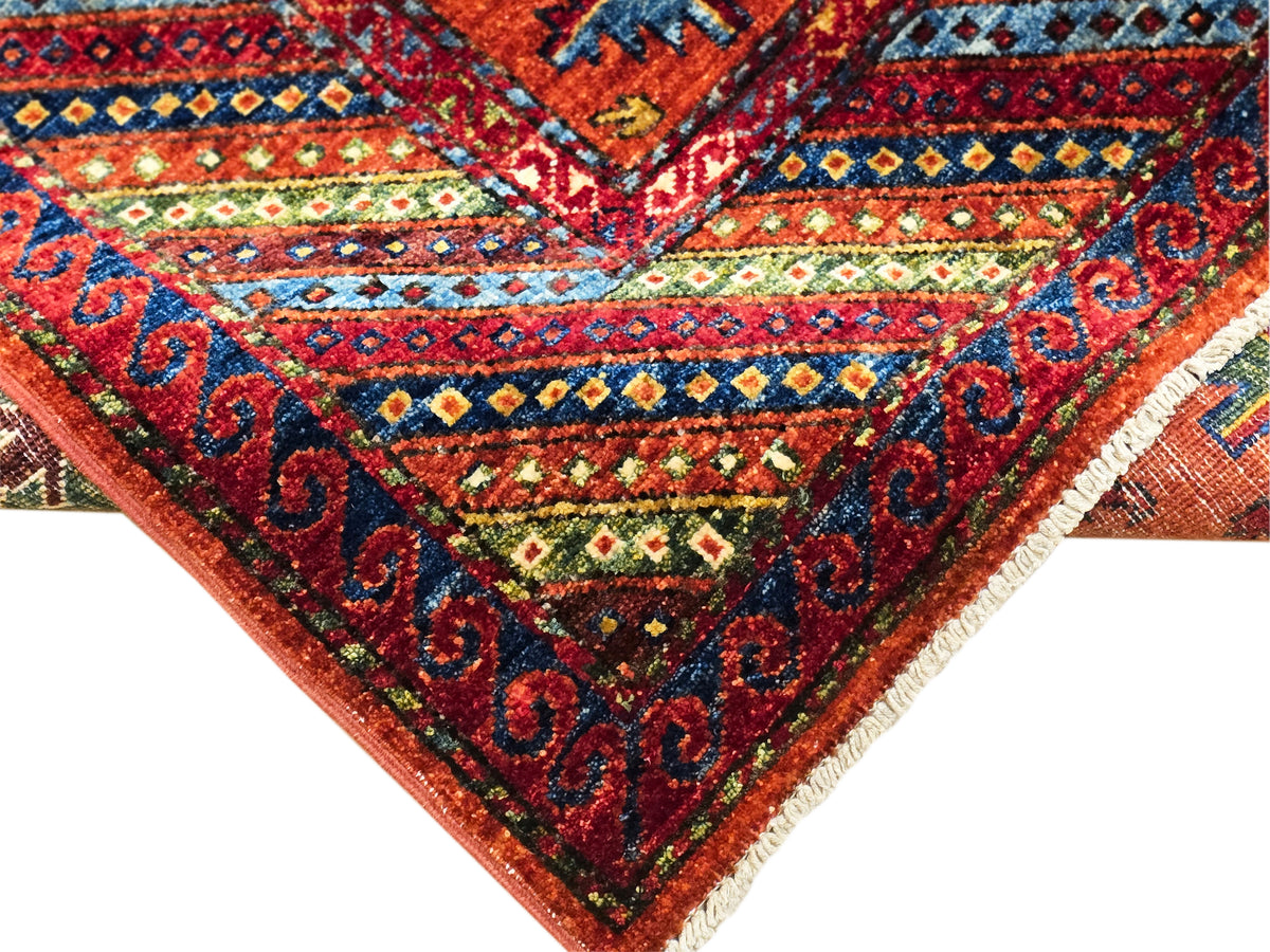 Rug corner close-up: red-orange ground with navy, teal, and green ornamental border