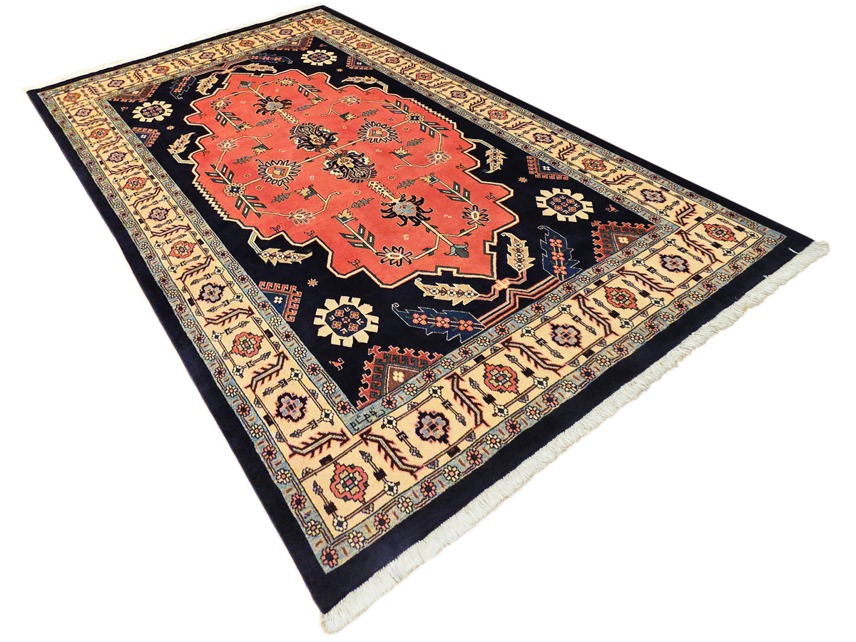 Ornate rectangular rug with orange-red center, dark navy border, cream decorative trim, fringe