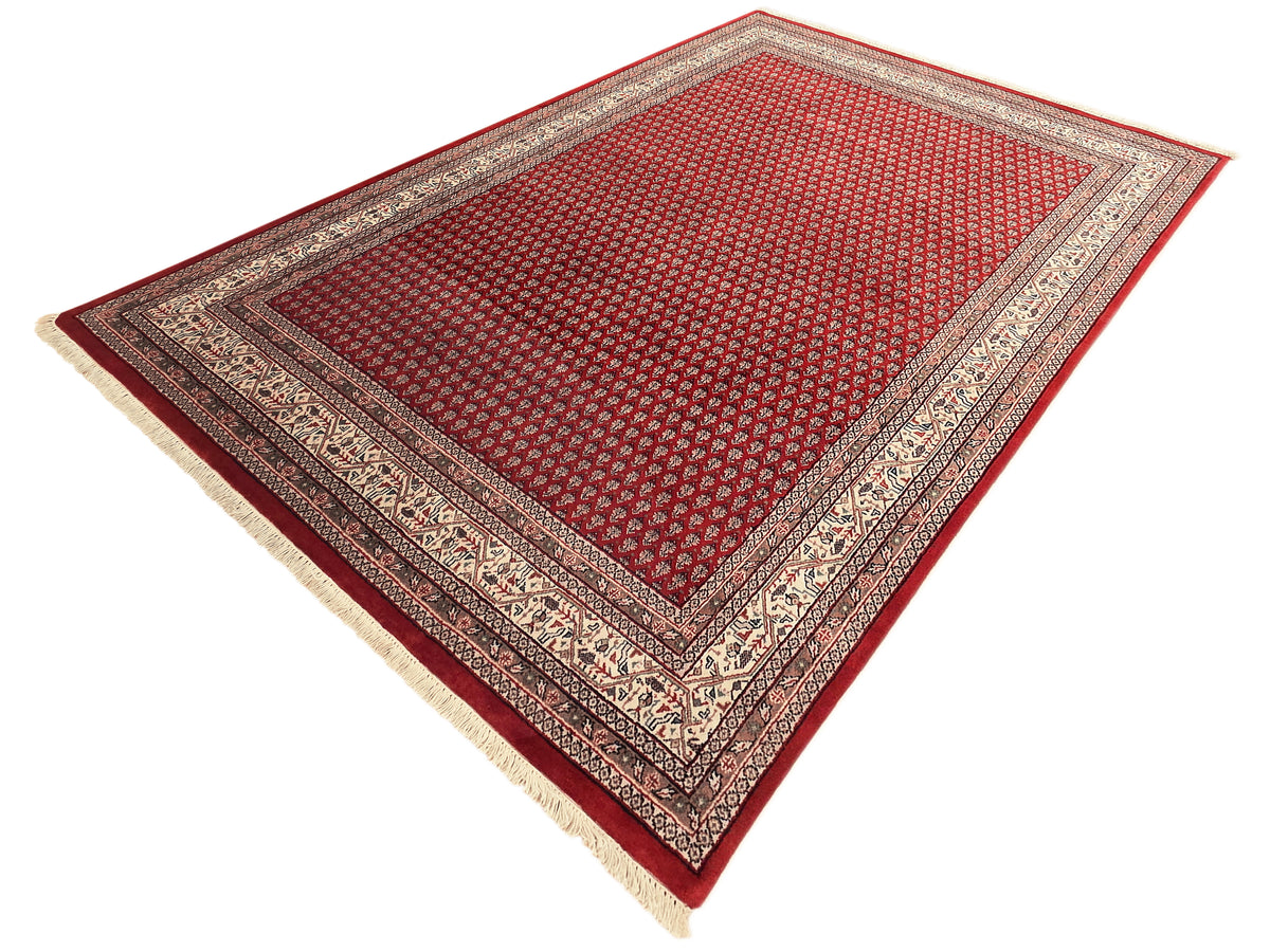 Red area rug corner view with patterned field and cream and dark border frame.