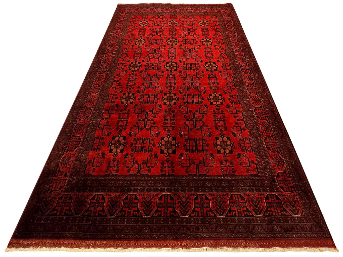 Red rug with central panel design, dark border bands, and tan fringe edges.