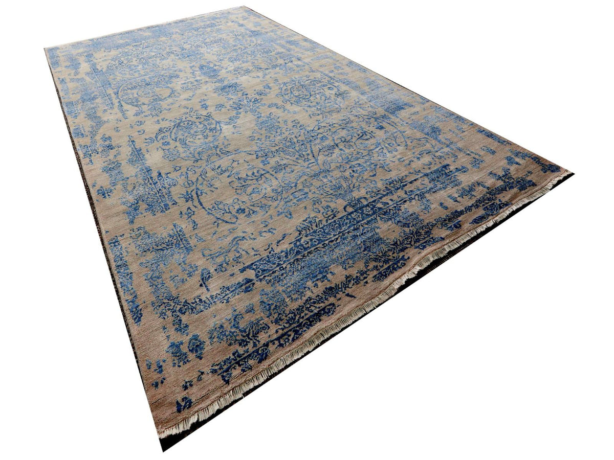 Diagonal view of rectangular area rug with blue distressed pattern on beige ground and fringe.
