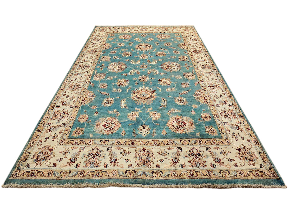 Turquoise rug with central floral motifs, ornate ivory border, and fringed perimeter