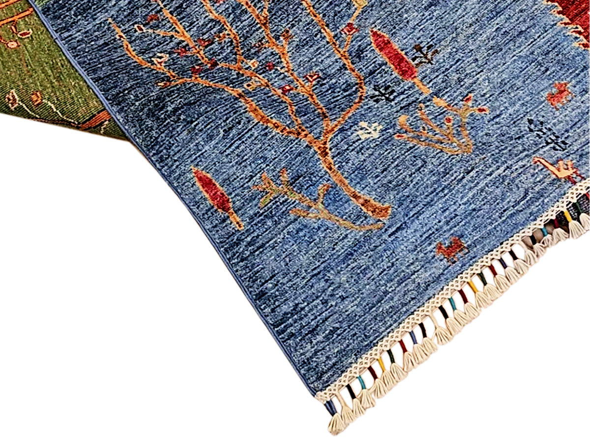 Corner view of blue rug with orange and red branch patterns and beige fringe edge.