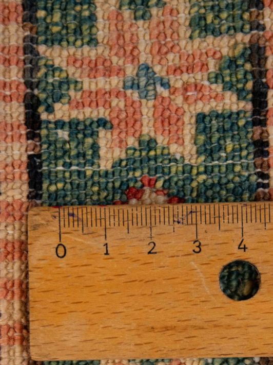 Close-up of red and teal geometric rug weave with ruler for scale