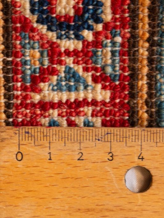 Kazak rug close-up: red, blue and gold knotted pile with ruler scale