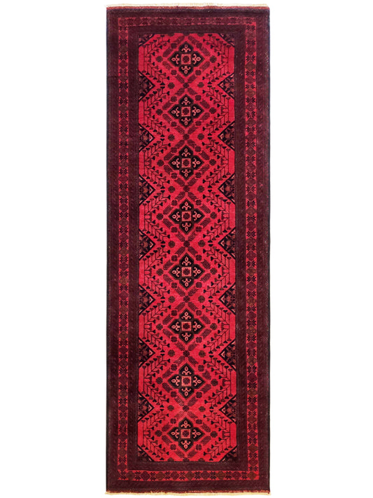 Narrow red rug with repeating geometric border and fringe on sides