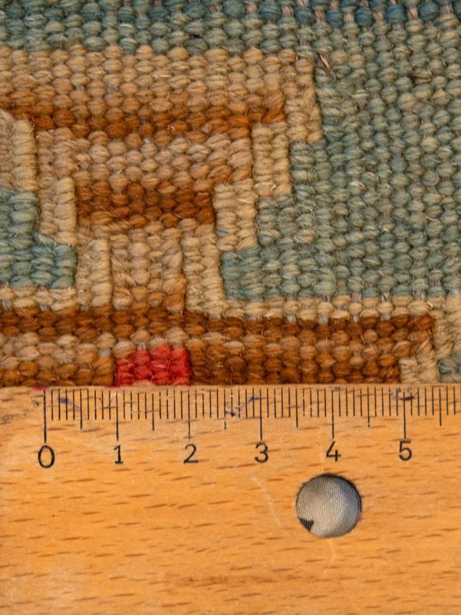 Close-up of multicolor kilim rug texture with geometric border; includes measuring tape